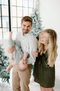 A young family of three pose for a family portrait session in a natural light studio with Kati Hewitt Photography